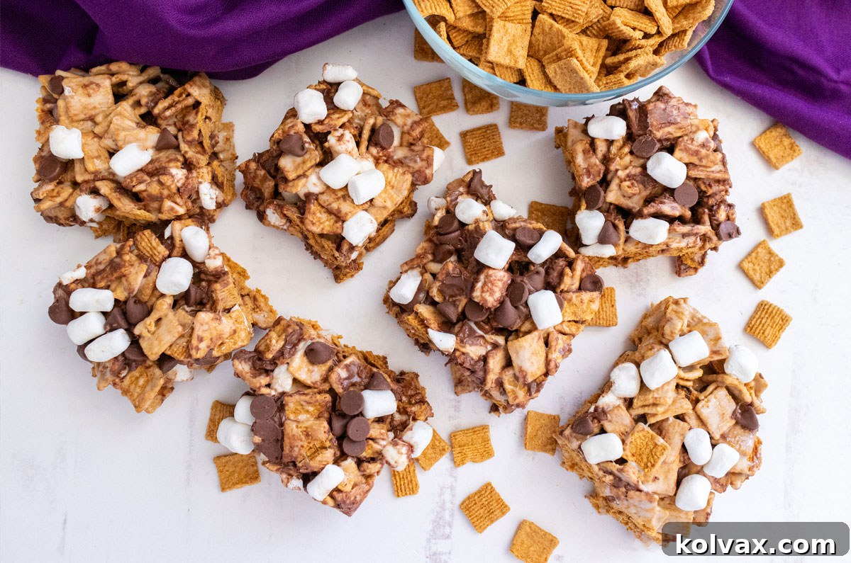 An overhead shot showcasing seven perfectly cut Golden Grahams S'mores Marshmallow Treats arranged on a white table, accompanied by a folded purple kitchen towel.