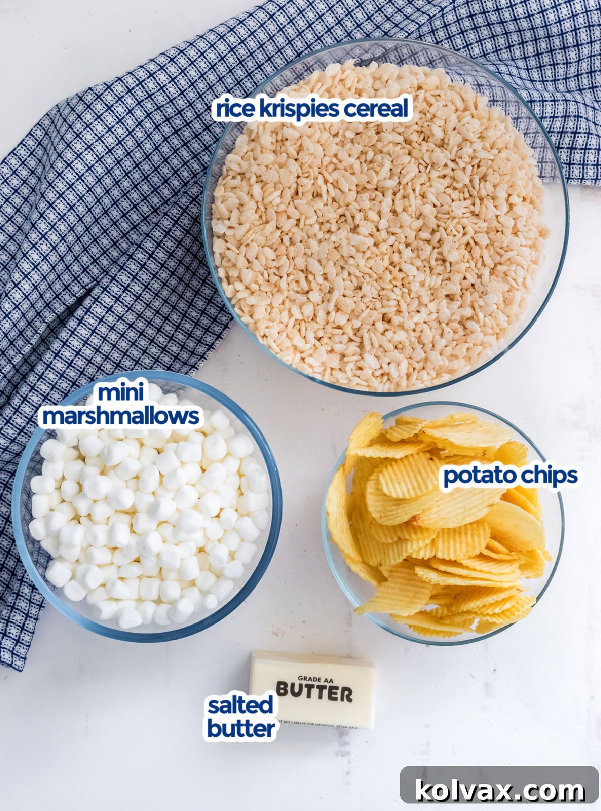 All the ingredients neatly laid out on a white surface, including butter, mini marshmallows, Rice Krispies cereal, and a bag of potato chips, ready to make Potato Chip Rice Krispie Treats.