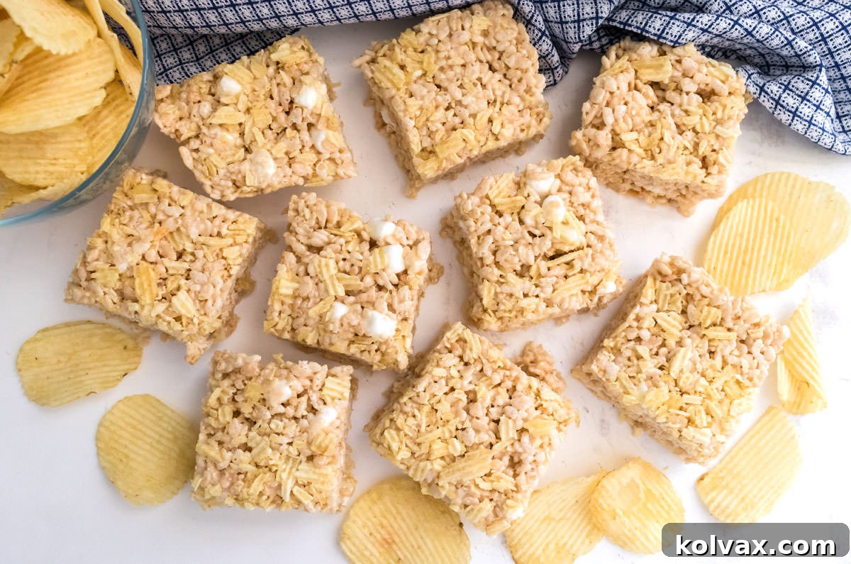 An overhead shot of nine perfectly cut Potato Chip Rice Krispie Treats artfully arranged on a white table, alongside a blue plaid kitchen towel, highlighting their appealing texture.