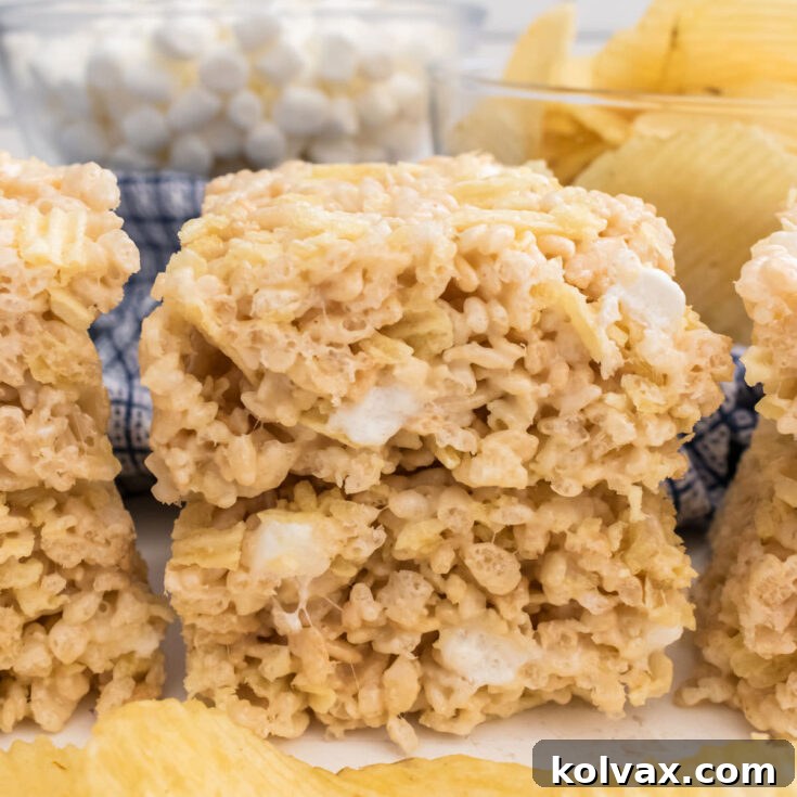 A batch of Potato Chip Rice Krispie Treats sitting on a white table in front of a handful of Ruffles Potato Chips, highlighting their sweet and salty appeal.