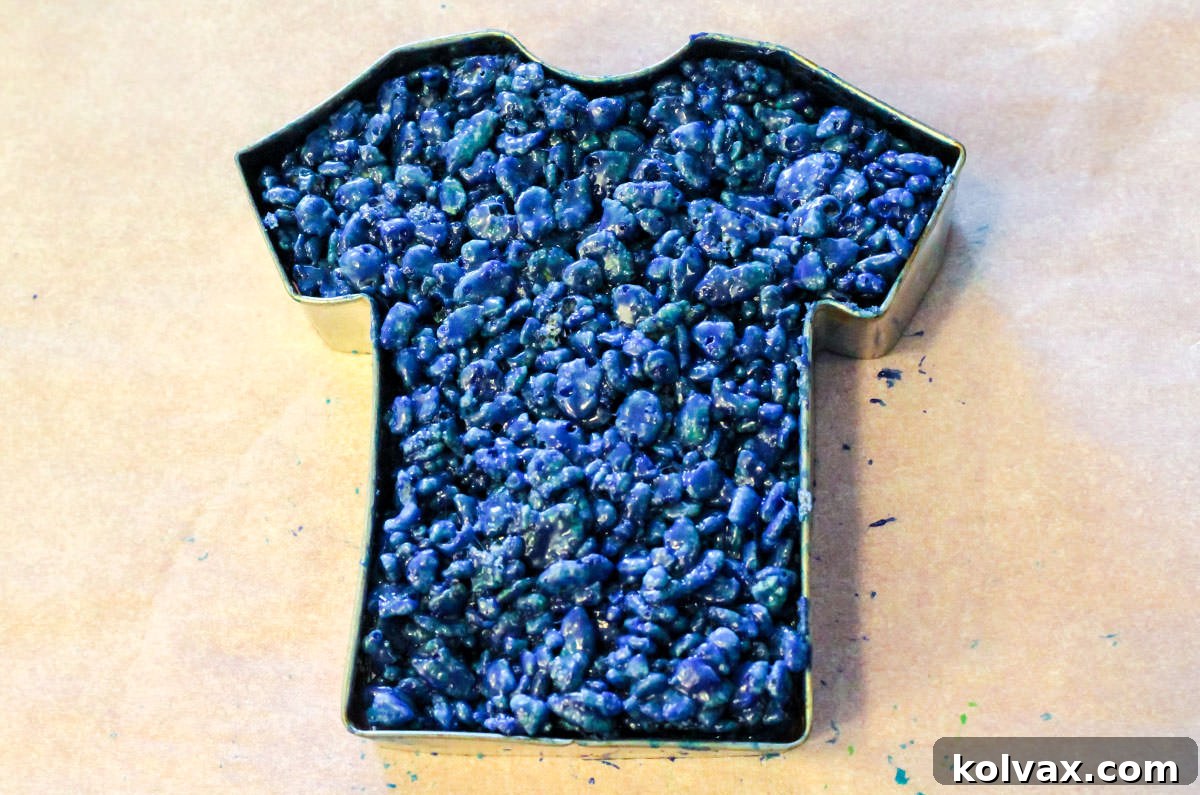 A close-up view of a football jersey-shaped cookie cutter filled with the vibrant Navy Blue Rice Krispie Treat mixture, perfectly molded and ready for cooling.