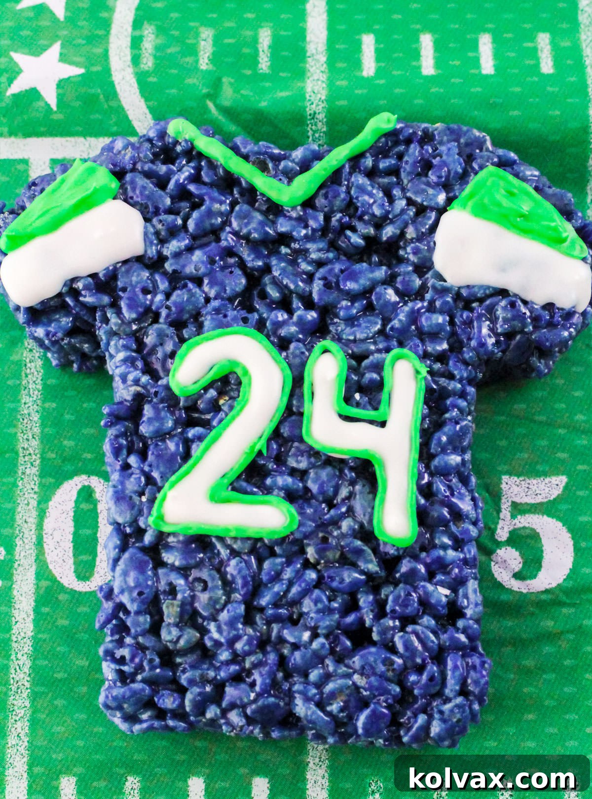 A close-up of a single Seattle Seahawks Rice Krispie Treat jersey, beautifully decorated and ready to be enjoyed, positioned on a football-themed tablecloth.