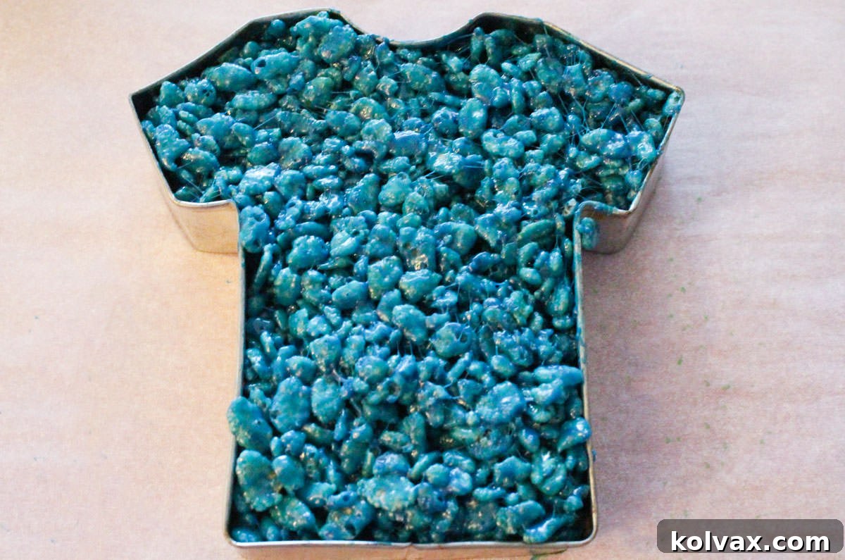 Closeup on a T-shirt shaped cookie cutter filled with blue Rice Krispie Treat mixture.
