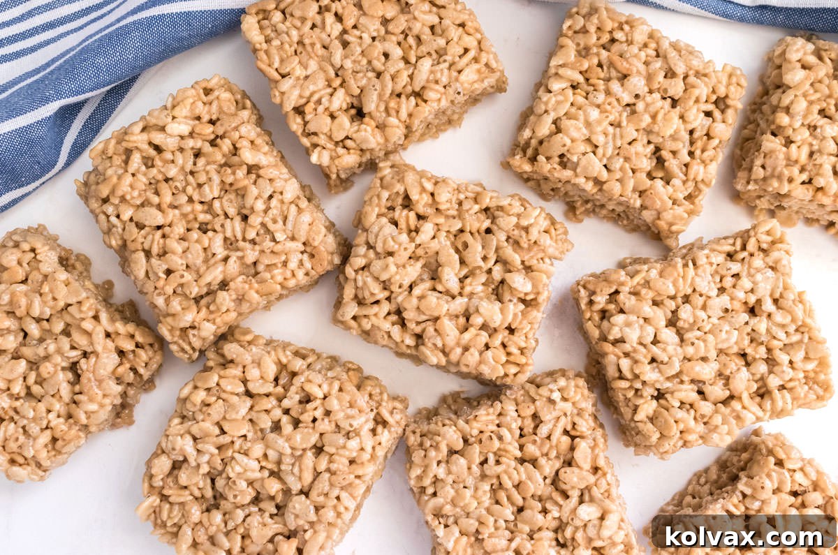 An overhead shot showcasing a beautifully arranged batch of Maple Rice Krispie Treats on a white table, accompanied by a blue kitchen towel, ready to be enjoyed.