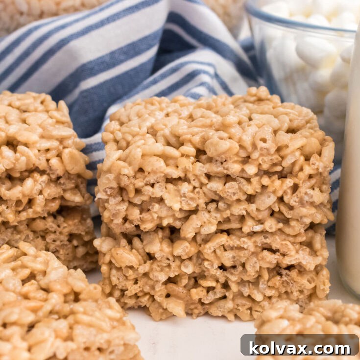 A stack of two Maple Rice Krispie Treats sitting on a white surface in front of a blue striped kitchen towel.