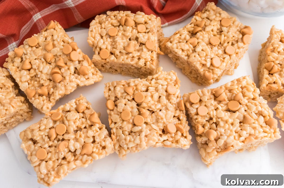 An overhead shot of perfectly cut Butterscotch Rice Krispie Treats arranged on a white table, accompanied by a burnt orange kitchen towel, ready to be served.