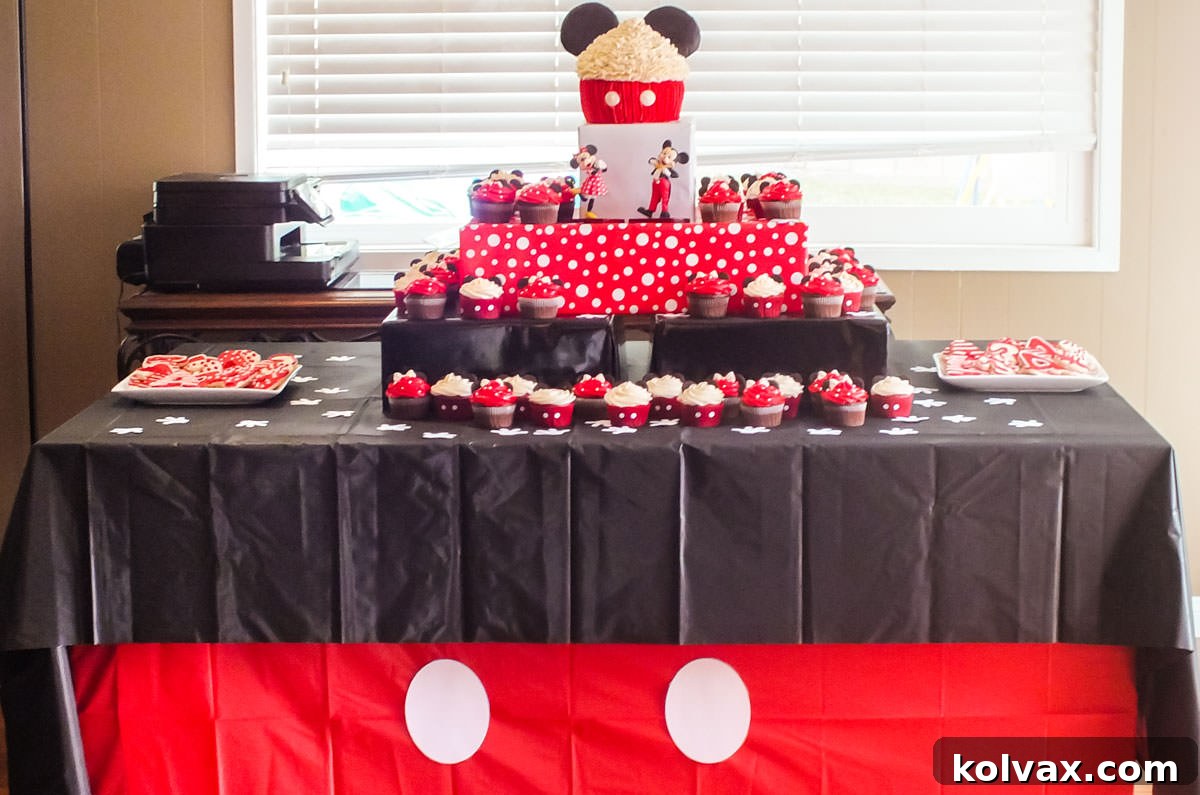 Mickey Mouse themed dessert table with a red and black tablecloth and a tiered cupcake stand.
