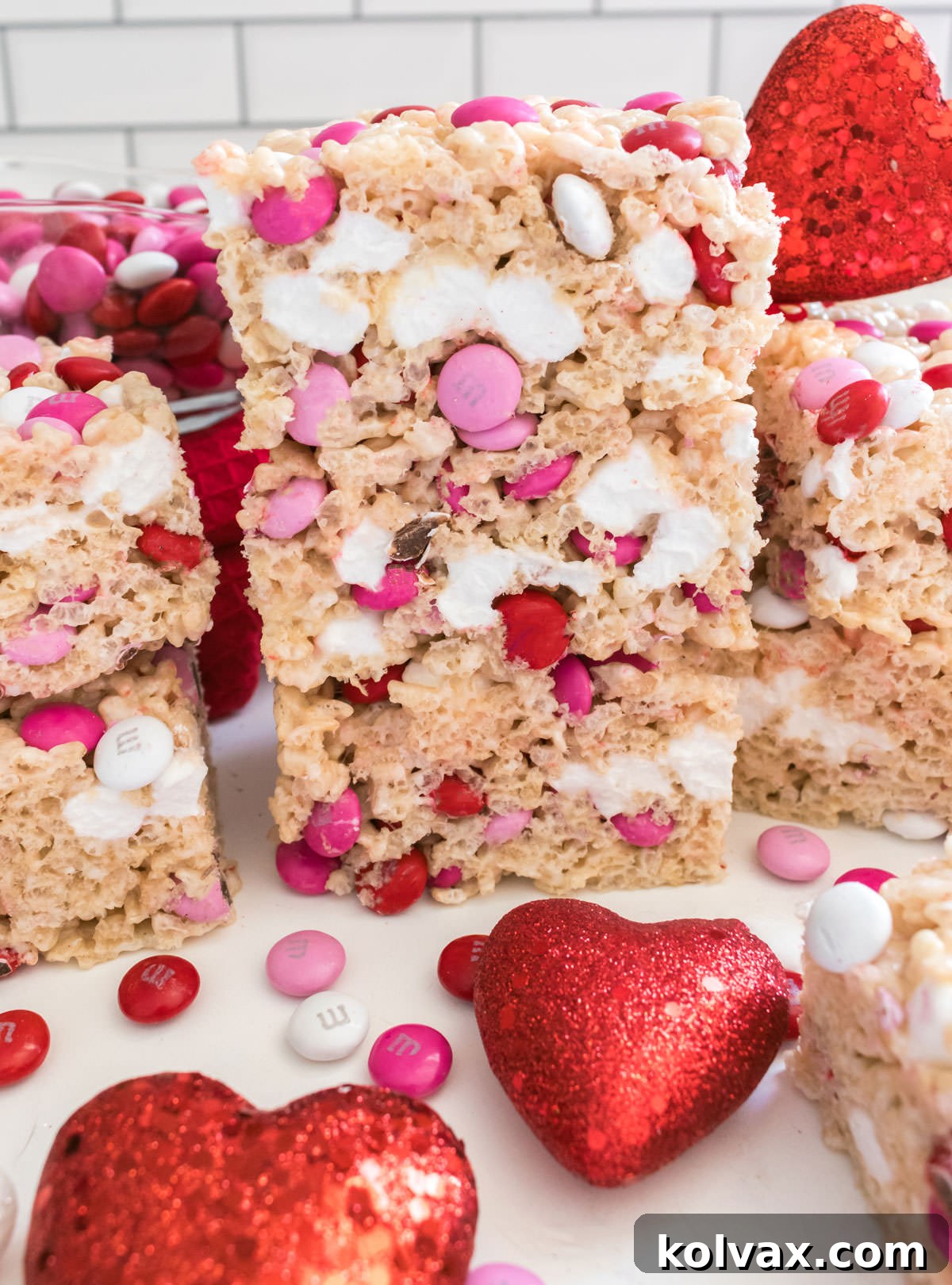 Sweetheart M&M Rice Krispie Bars 9 A delightful close-up of three Valentine's Day M&M Rice Krispie Treats stacked on a white surface, artfully decorated with small heart accents, emphasizing their inviting and festive appearance.