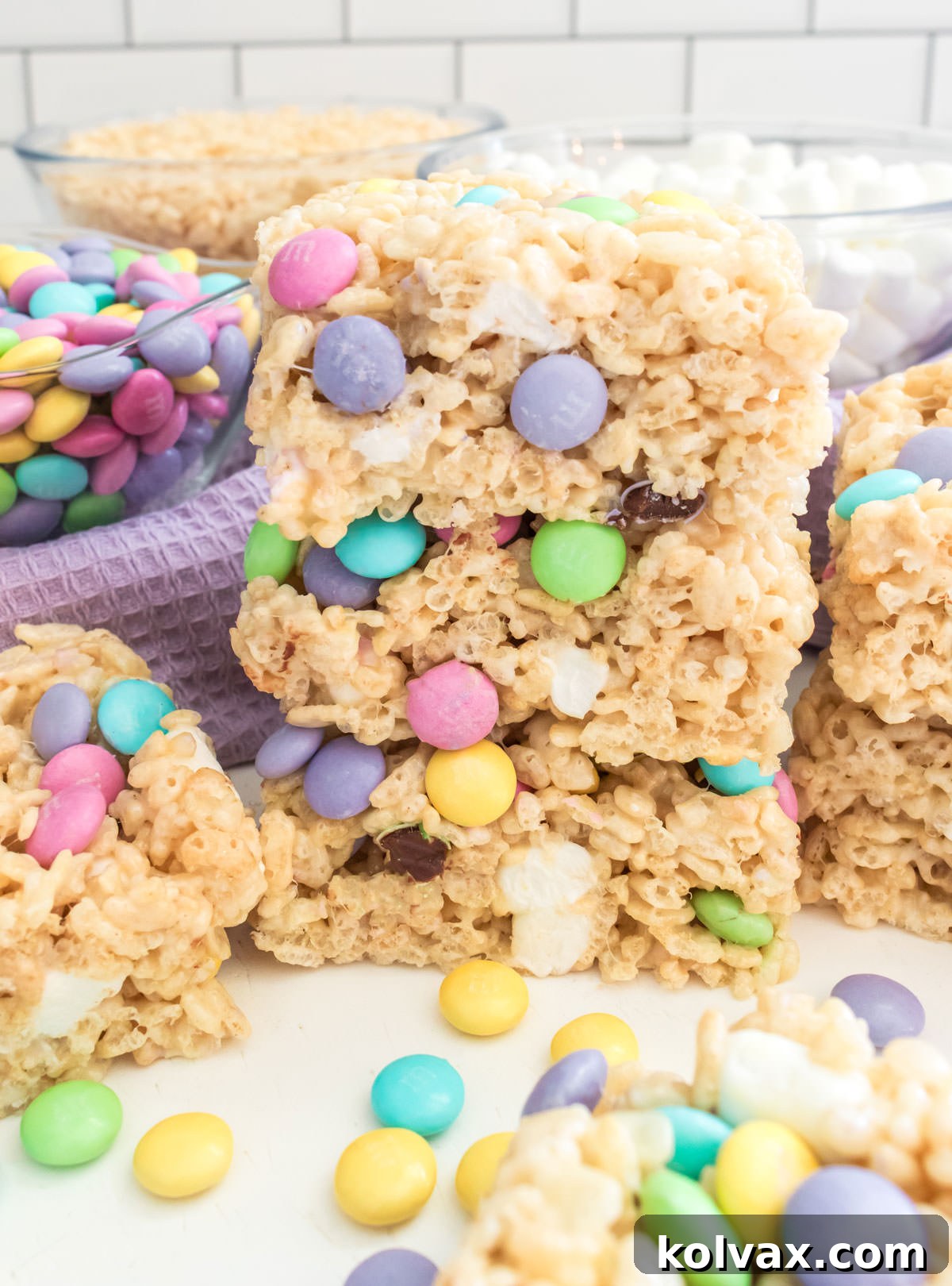 A beautiful close-up of a stack of three Springtime M&M Rice Krispie Treats, highlighting their soft texture and colorful pastel M&M's, artfully arranged on a white table.