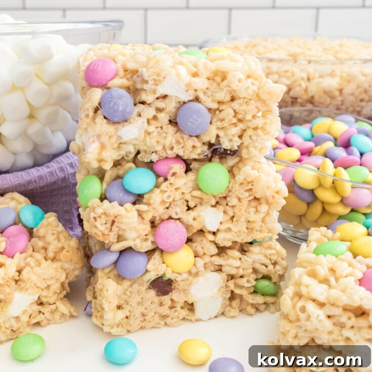 A stack of three vibrant Springtime M&M Rice Krispie Treats, with extra mini marshmallows and Rice Krispie cereal in the background.