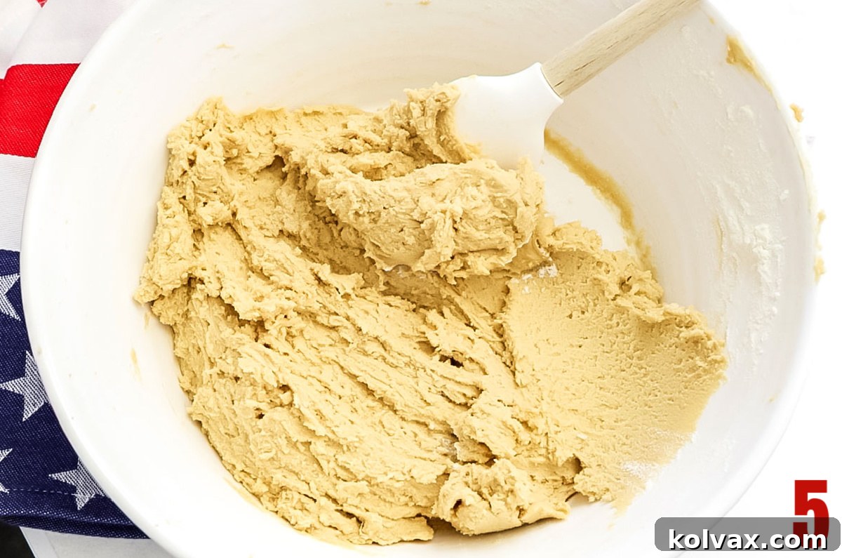 Large white bowl filled with perfectly mixed chocolate chip cookie dough and a rubber spatula resting inside.