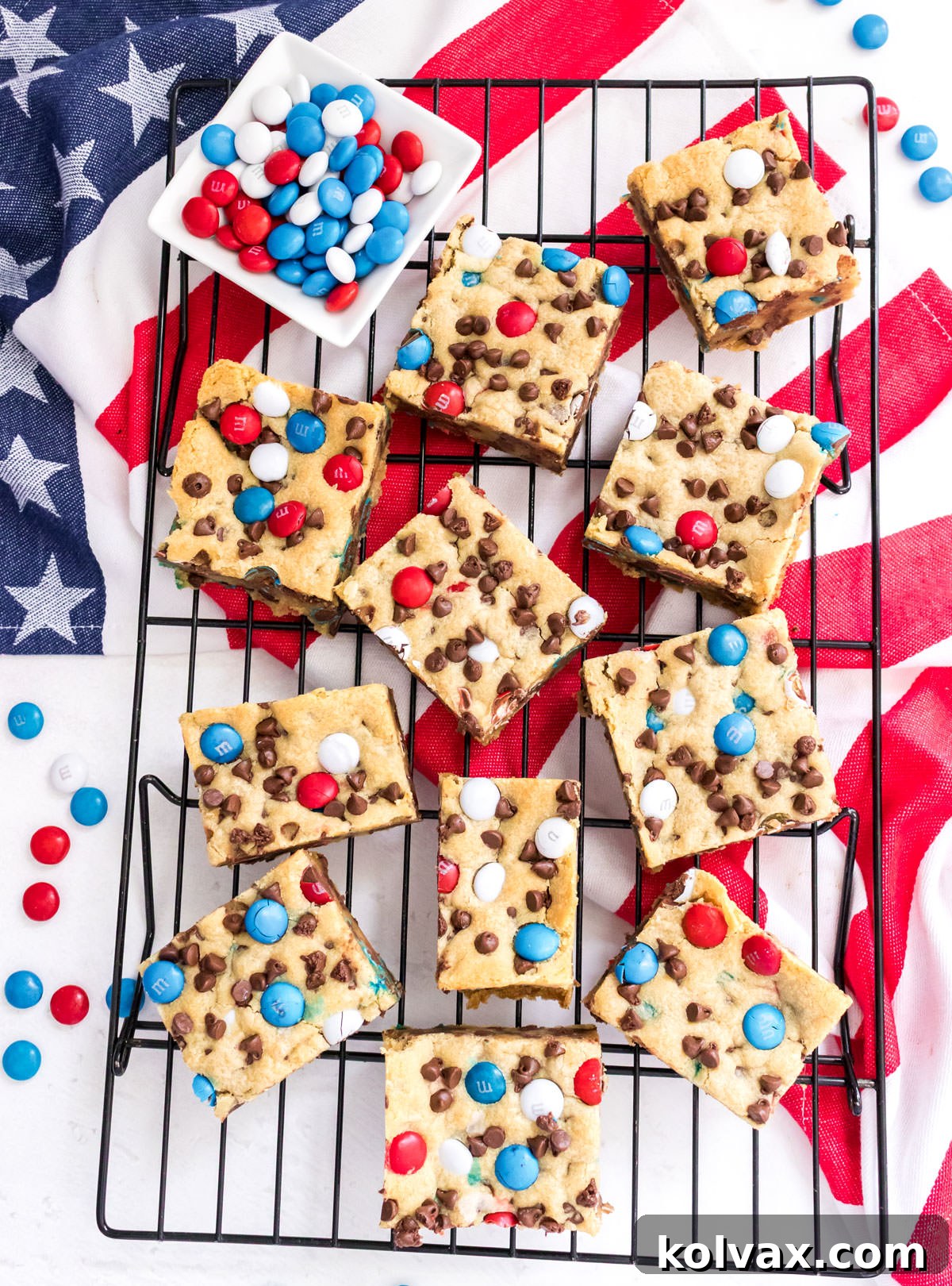 Overhead shot of a batch of Patriotic M&M Chocolate Chip Cookie Bars laying on a cooling rack over an American Flag Kitchen Towel, perfectly baked and ready to be sliced.
