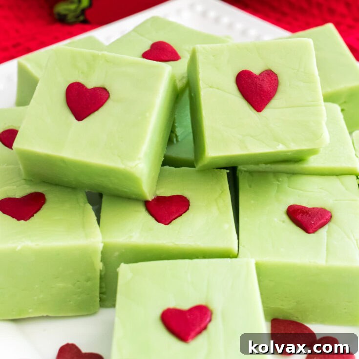 Closeup on a batch of Easy Grinch Fudge sitting on a white plate surrounded by heart sprinkles, ready to be served.