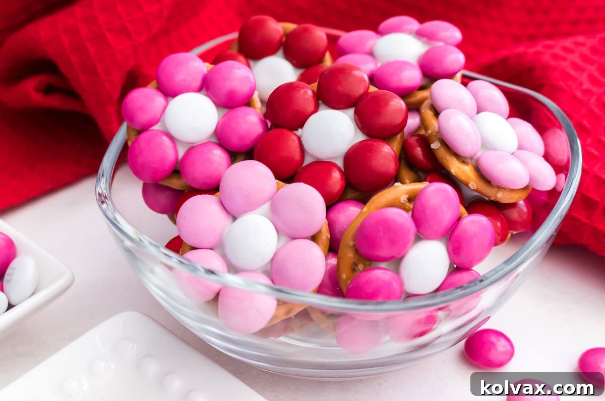 A small glass bowl overflowing with beautifully arranged Rose Garden Flower Pretzel Bites, set against a soft red fabric backdrop, showcasing their festive colors and delicate design.