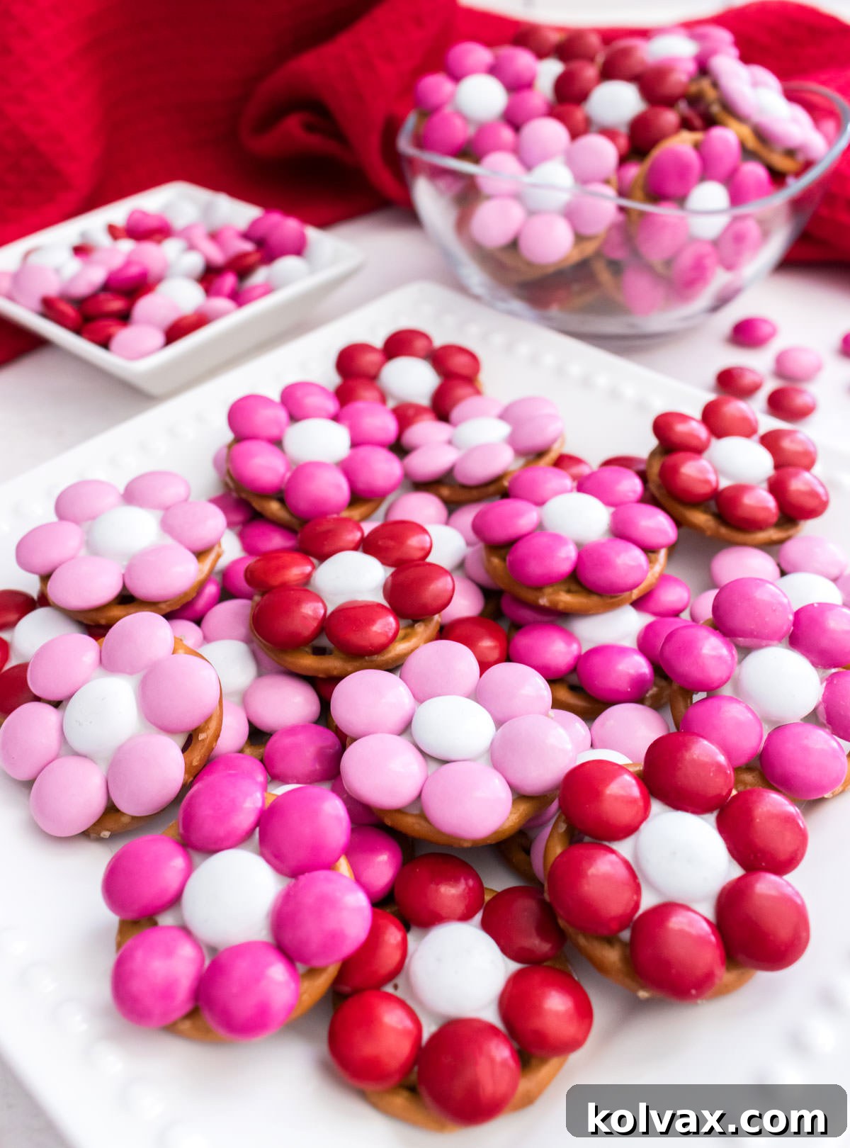 A beautifully decorated party table featuring Rose Garden Flower Pretzel Bites displayed elegantly on a white dessert plate and in a small glass bowl, surrounded by other festive elements.
