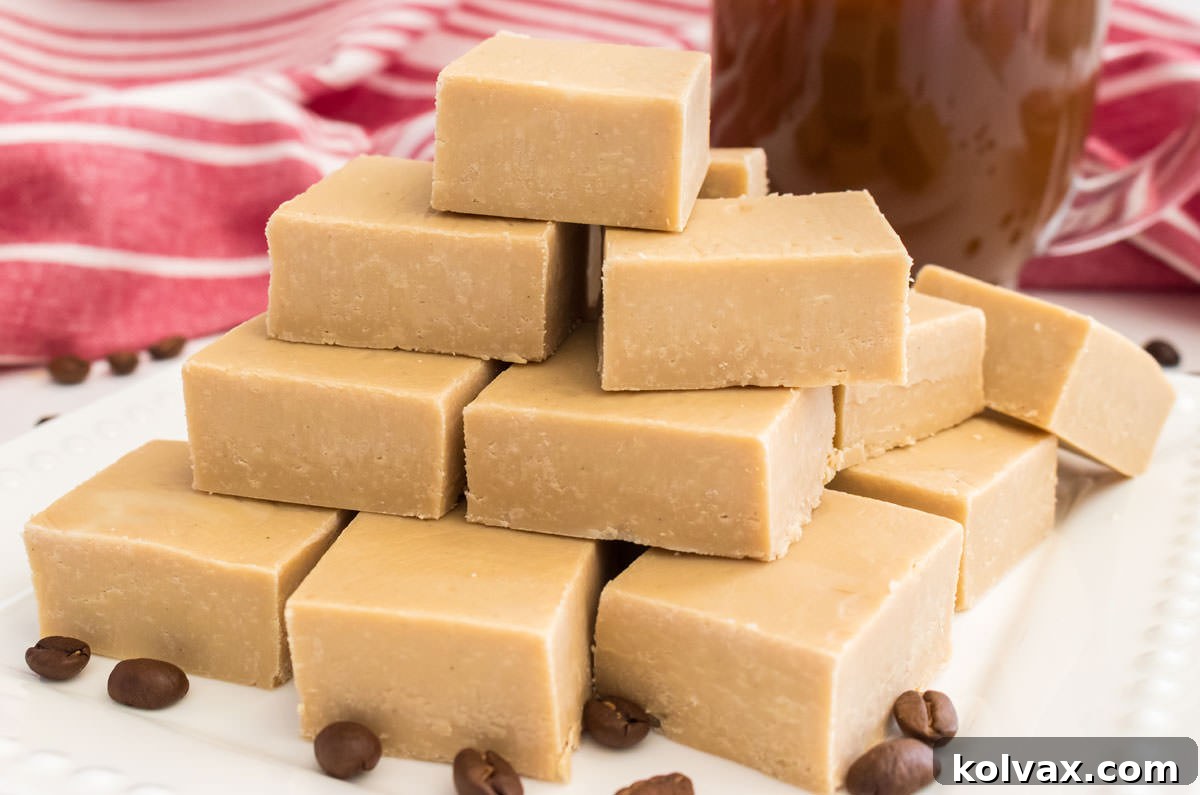 Closeup on a stack of Easy Coffee Fudge sitting on a white dessert plate next to a cup of coffee. The fudge has a smooth texture and a light brown color.