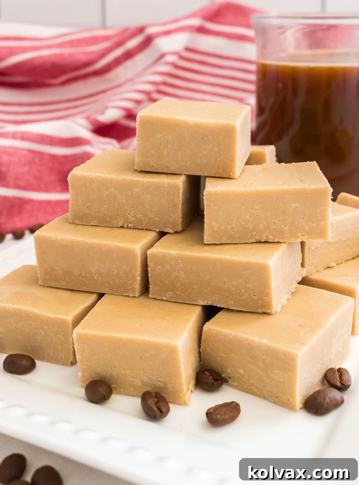 A pyramid of Easy Coffee Fudge sitting on a white dessert plate next to a glass mug filled with Coffee, showcasing its appealing texture.
