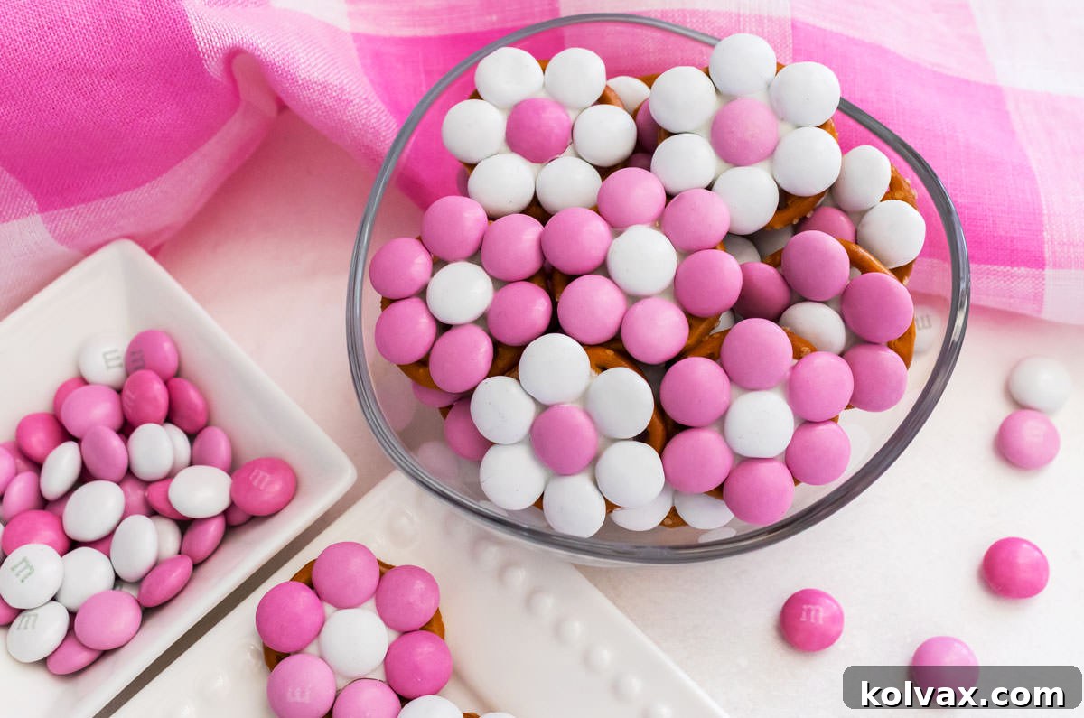 Closeup of a small glass bowl overflowing with Pretty in Pink Flower Pretzel Bites, artfully arranged on a pristine white table.