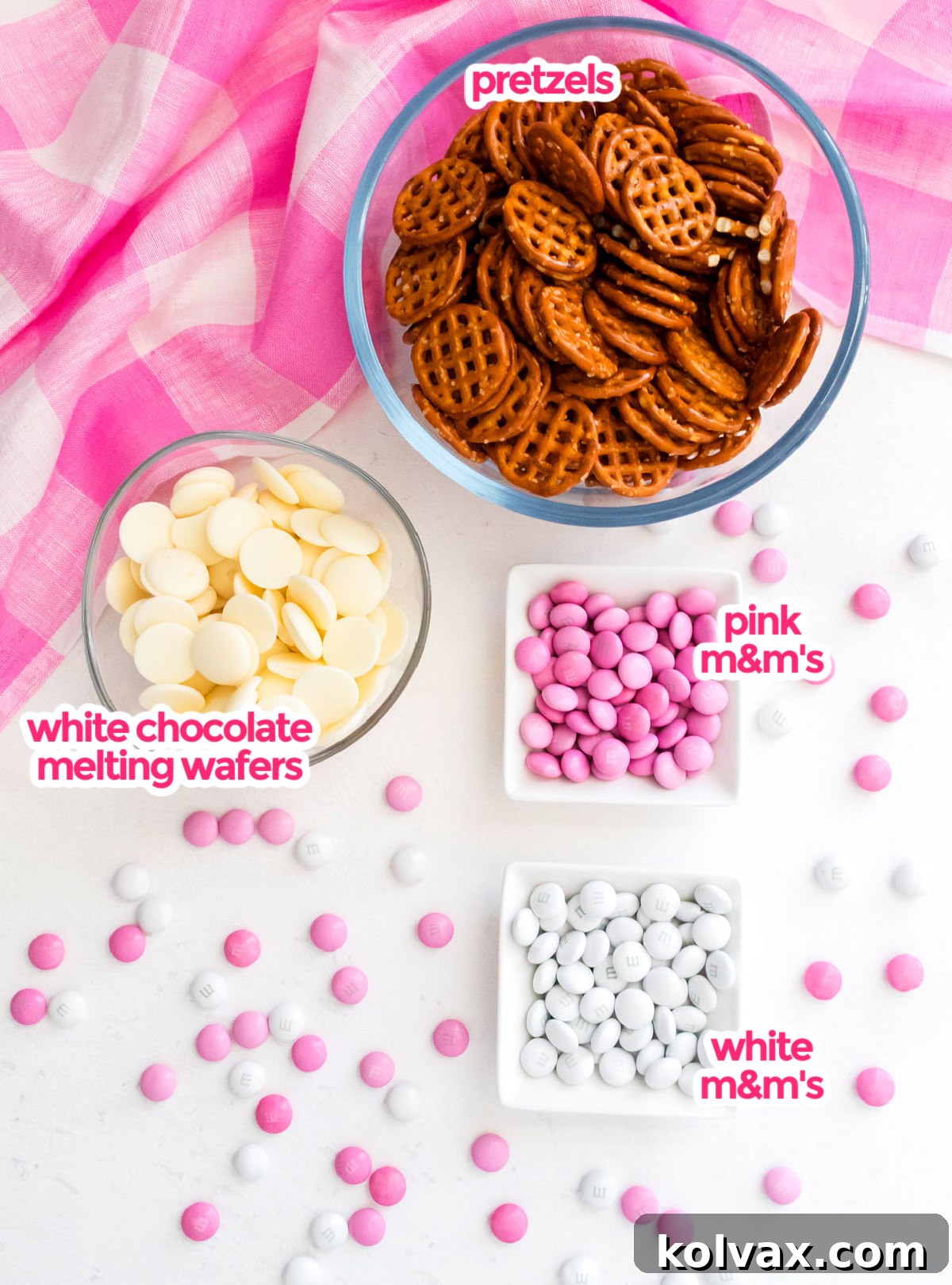 A flat lay showing all three essential ingredients for Pretty in Pink Flower Pretzel Bites: a bag of square pretzels, white candy melts, and pink and white M&M's.
