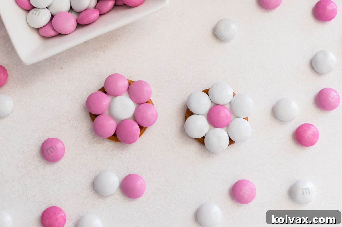 A close-up of two finished Pretty in Pink Flower Pretzel Bites on a white table, surrounded by scattered pink and white M&M's, highlighting their vibrant design.