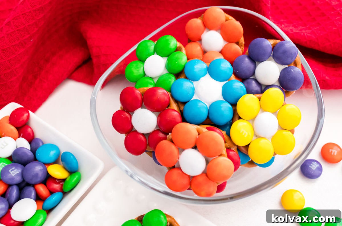 Closeup on a clear glass ramekin filled with Over the Rainbow Flower Pretzel Bites sitting on a white table in front of a red kitchen towel.