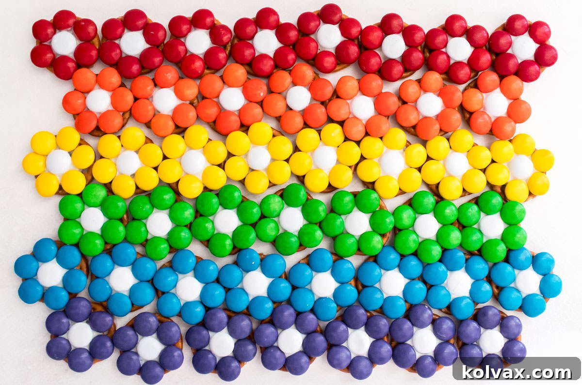 A batch of Red, Orange, Yellow, Green, Blue and Purple Over the Rainbow Flower Pretzel Bites arranged in rows in the shape of a Rainbow.