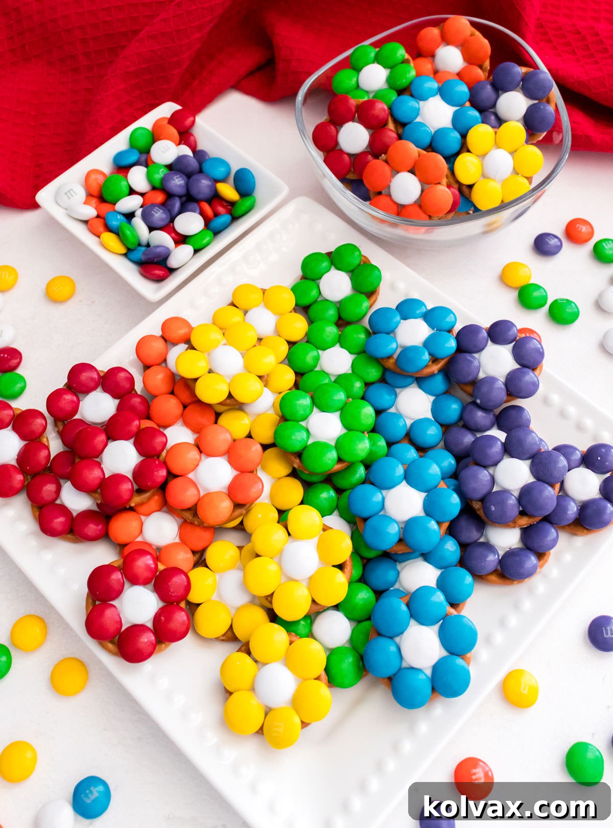 Closeup on a white dessert table featuring Over the Rainbow Flower Pretzel Bites displayed on a dessert plate and a clear glass bowl.