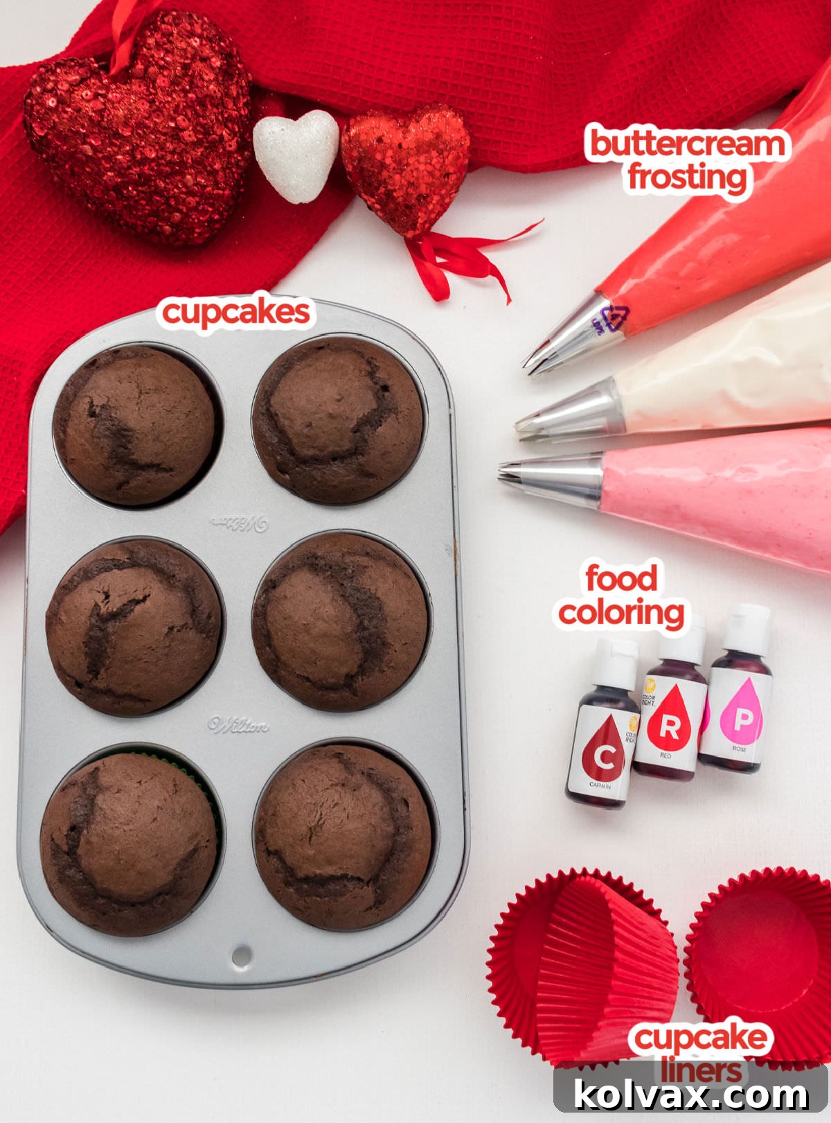 All the ingredients you will need to make Valentine's Day Cupcakes including baked cupcakes, prepared buttercream frosting, various food colorings, and cupcake liners in a festive setting.