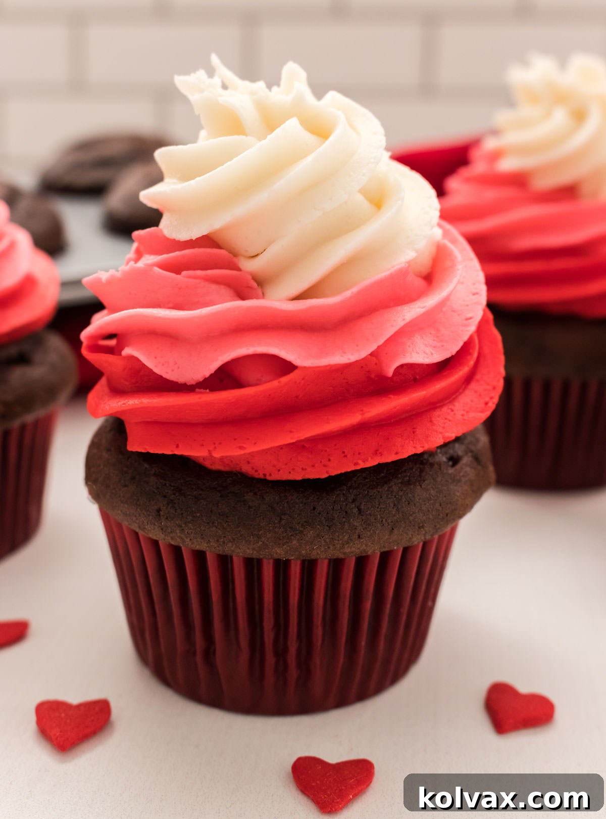 Close up of a single Valentine's Day Cupcake with a vibrant three-color swirl of red, dark pink, and white buttercream frosting, adorned with tiny heart sprinkles.