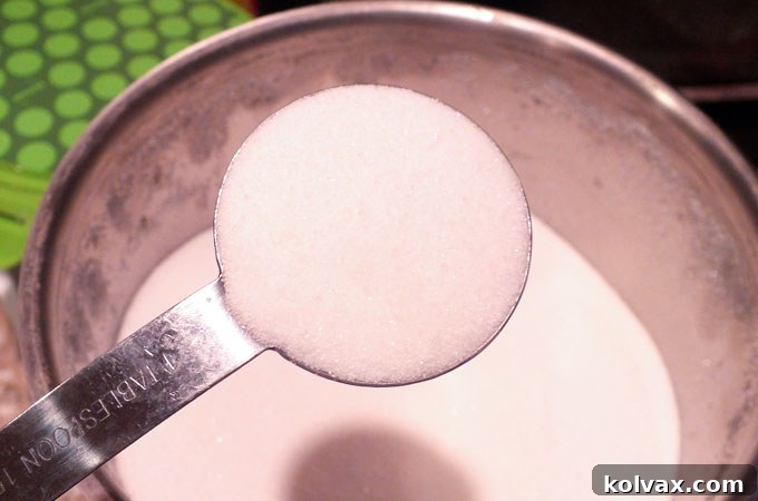 Adding white granulated sugar to the milk in the saucepan, ready to sweeten the vanilla milk.