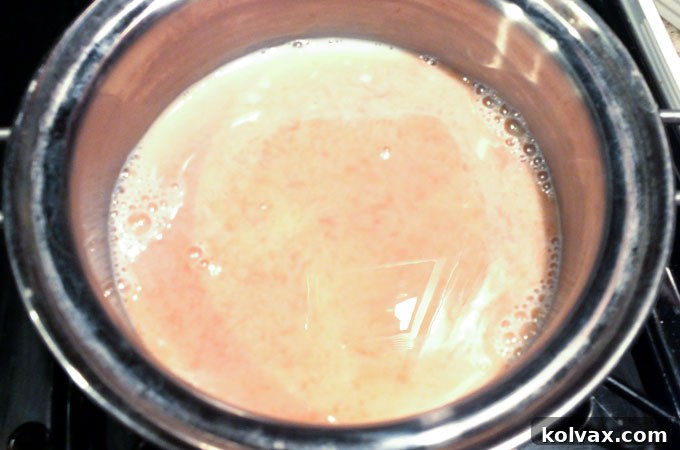 Pouring vanilla extract into the milk and sugar mixture in the saucepan for rich flavor.