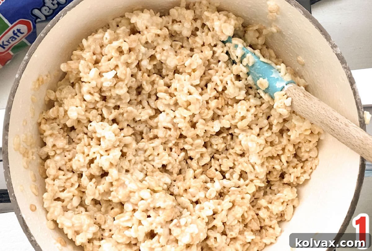 Closeup on a pristine white sauce pan filled with the warm, gooey Rice Krispie Treat mixture, being stirred gently with a white wooden spoon, capturing the perfect texture.