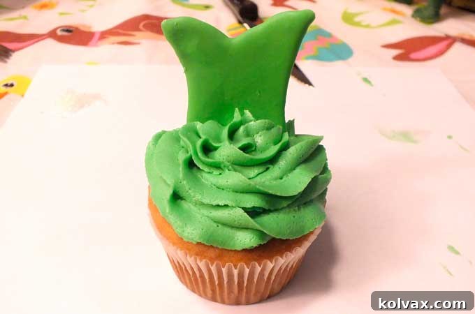 Gently pressing a royal icing Tinkerbell dress topper into the frosted cupcake.