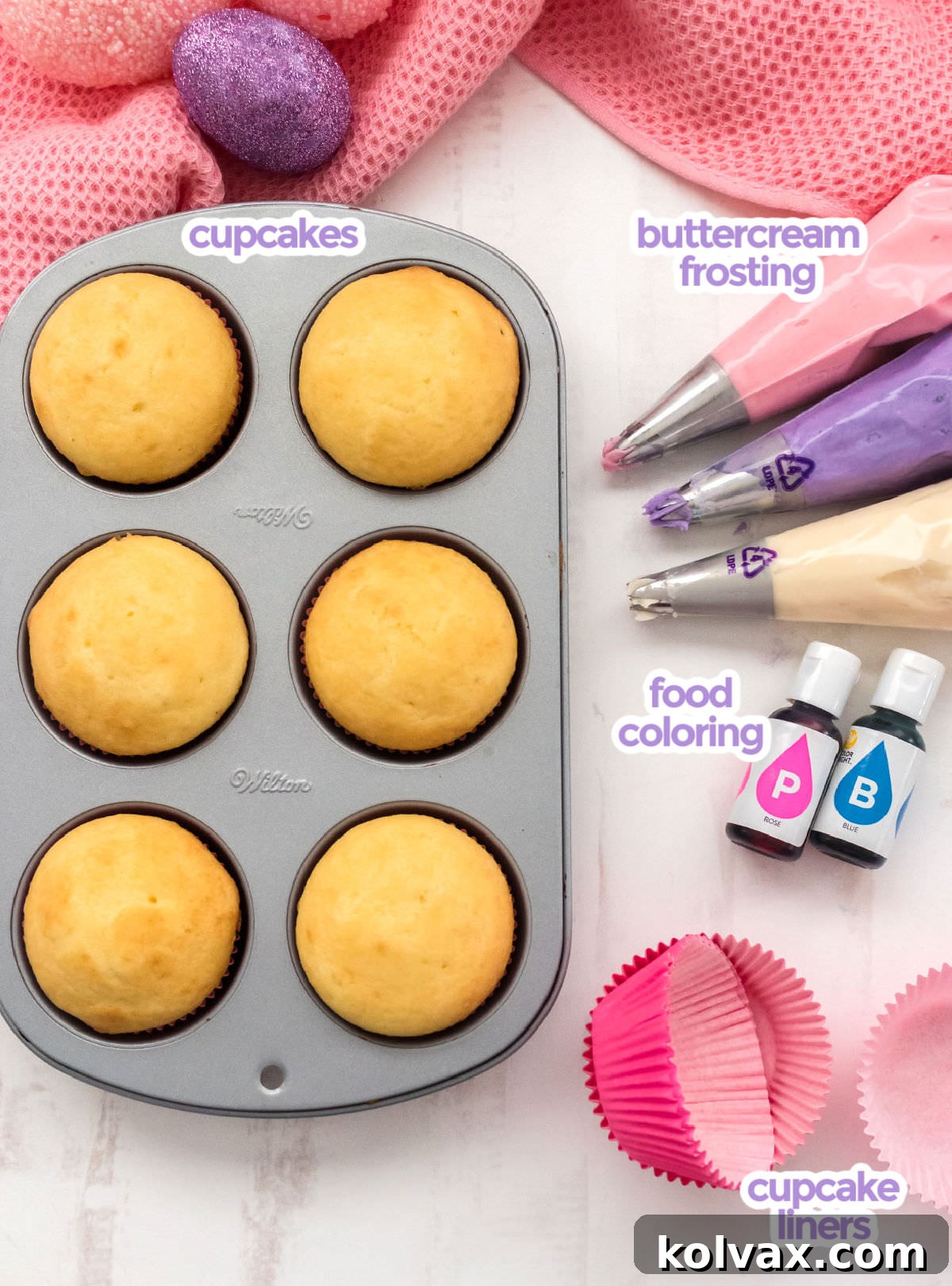 A comprehensive overhead shot displaying all the necessary ingredients to bake Easter Cupcakes, including baked vanilla cupcakes, vibrant purple, pink, and white frosting, various food colorings, and an assortment of cupcake liners, all laid out on a clean white surface.