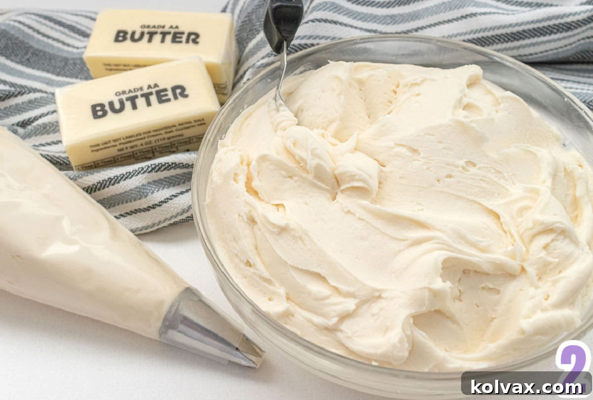 A clear glass mixing bowl brimming with freshly made buttercream frosting sits beside a piping bag filled with more frosting and two sticks of softened butter, illustrating the key components for delicious decoration.