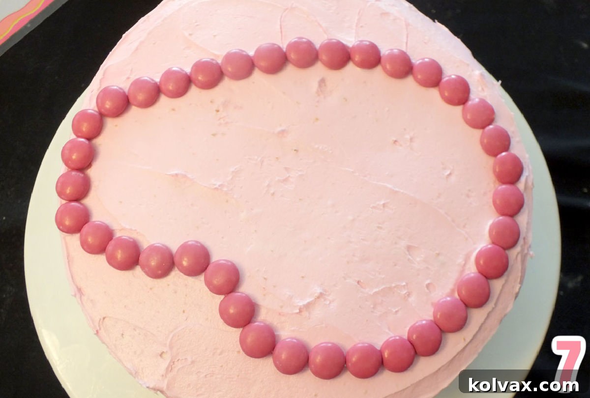 Closeup on the top of a cake frosted pink with the outline of Peppa Pig's face made with Pink M&M's.