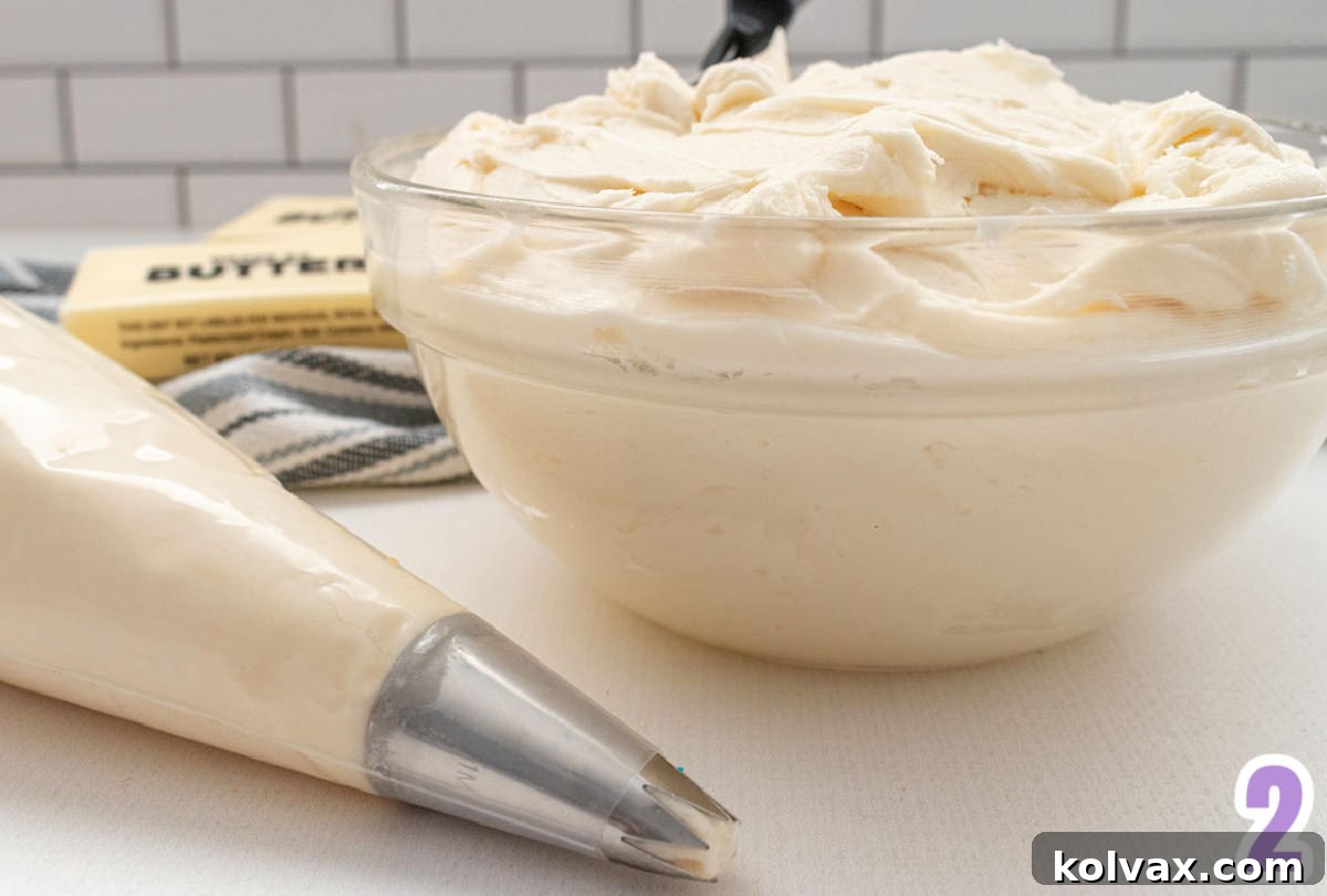 Closeup on a glass bowl filled with buttercream frosting sitting next to sticks of butter and a decorating bag filled with frosting.
