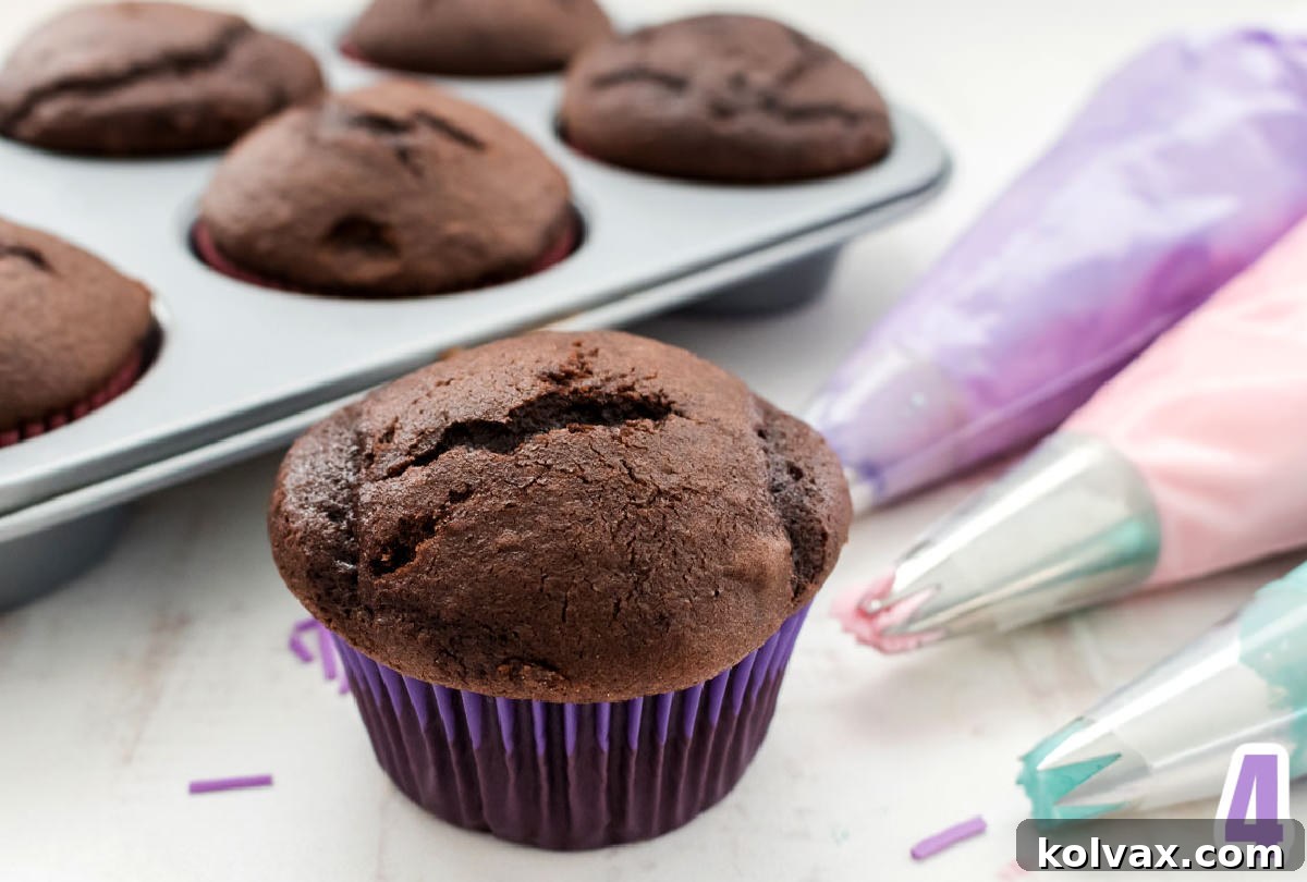 Chocolate cupcake in a purple cupcake liner sitting in front of a tin of cupcakes and buttercream frosting in decorating bags.