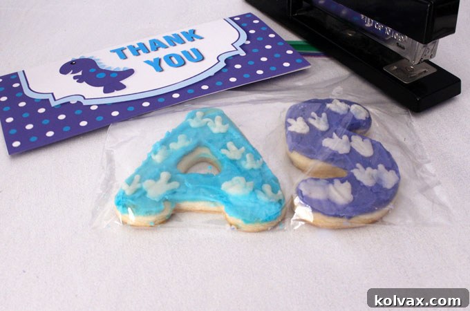 Assembling Dinosaur Party Thank You Cookies: Two decorated cookies in a sandwich bag, sealed with a stapled custom label.