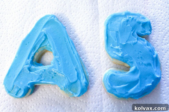 Frosting 'A' and '5' sugar cookies with vibrant blue and purple buttercream, forming the base for dinosaur decorations.