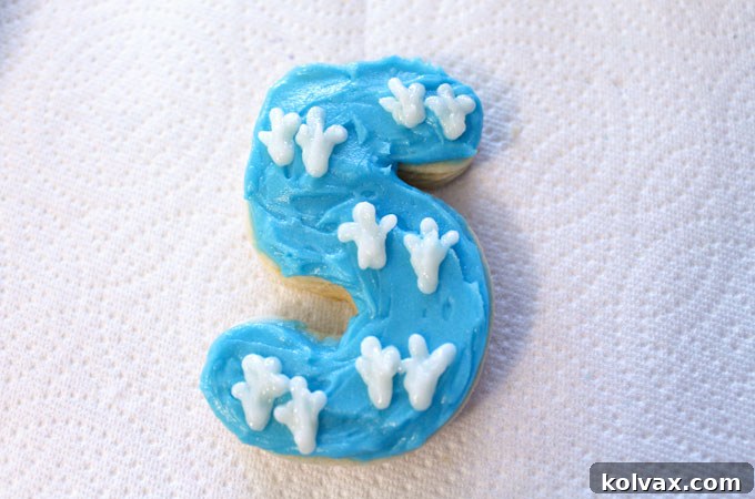 Variety of decorated sugar cookies with blue and purple frosting and white dinosaur footprints.