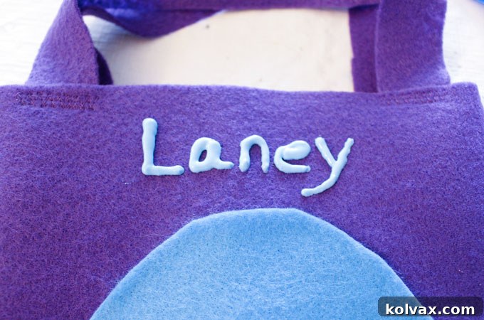 Personalizing each dinosaur party favor bag by adding the names of party-goers using vibrant puffy paint, making each bag a unique keepsake.