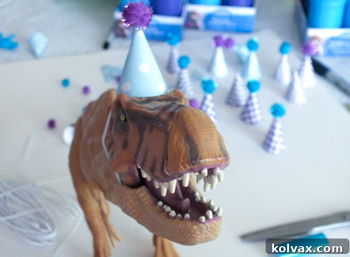 Gluing a small yarn pom-pom to the top of a DIY dinosaur party hat.