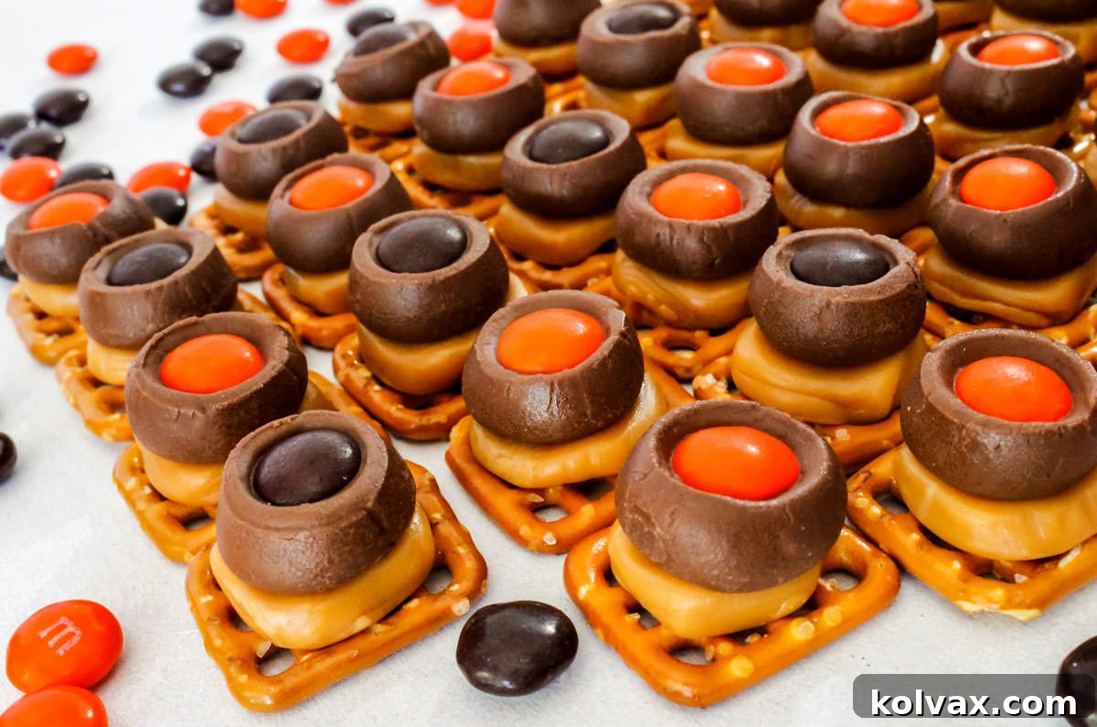 Spooky Salty Sweet Pretzel Delights 2 A close-up view of Halloween Chocolate Caramel Pretzel Bites, artfully arranged on a pristine white surface, surrounded by festive orange and brown M&M's, inviting you to take a bite.
