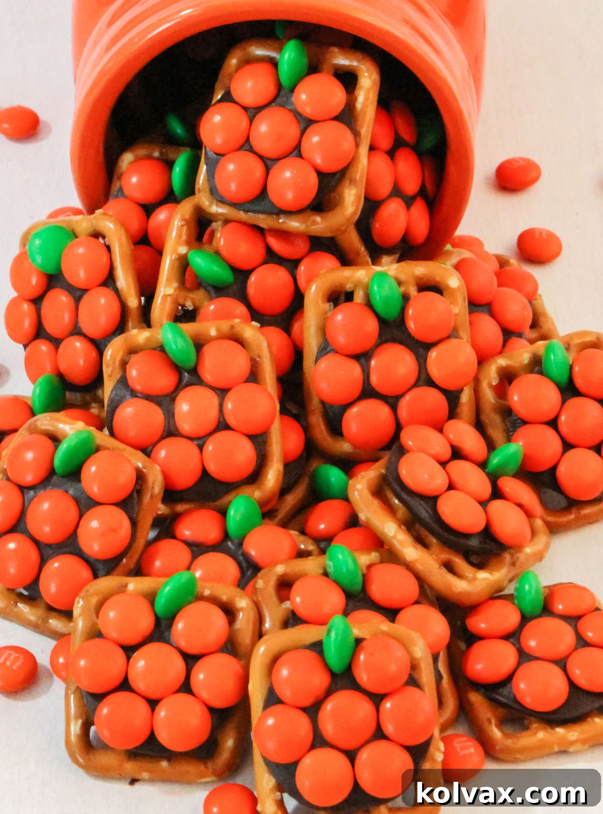 Closeup on Pumpkin Pretzel Bites spilling out of an orange mason jar onto a white table.
