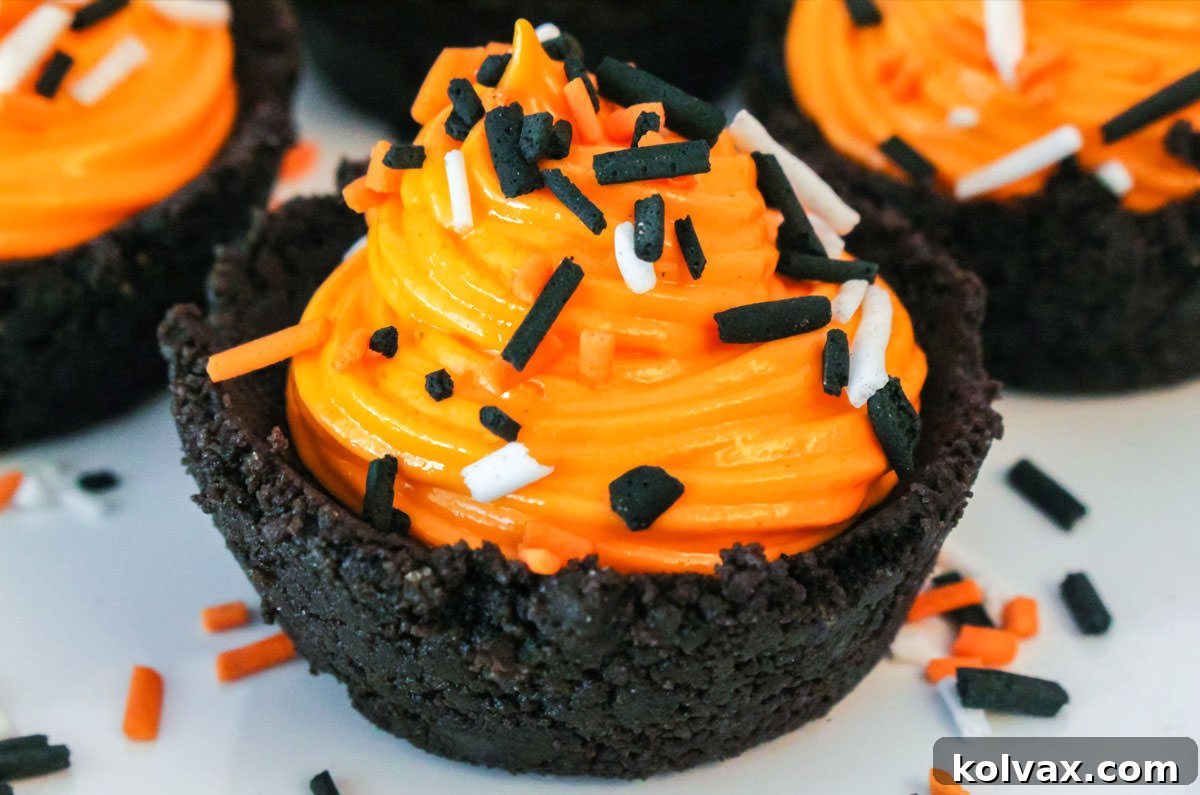 Close-up of a perfectly crafted Halloween Oreo Cookie Cup, showcasing its dark cookie crust, orange marshmallow cream filling, and colorful Halloween sprinkles, sitting on a white surface.
