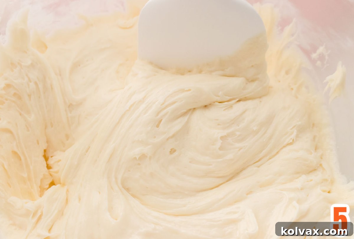 A clear glass bowl filled with fluffy, homemade Marshmallow Cream Frosting, ready to be used for decorating Halloween treats.