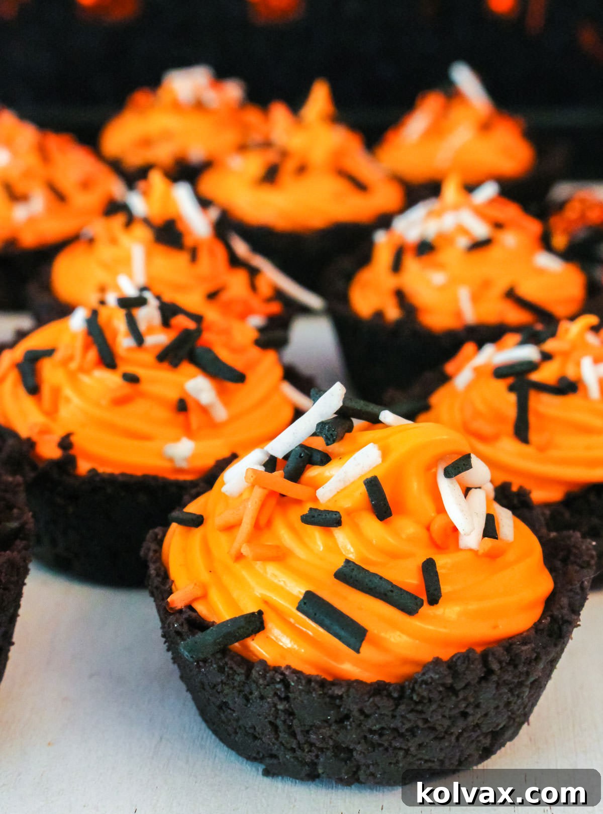 A batch of vibrantly decorated Halloween Oreo Cookie Cups with orange marshmallow cream and colorful sprinkles, arranged neatly on a white table.