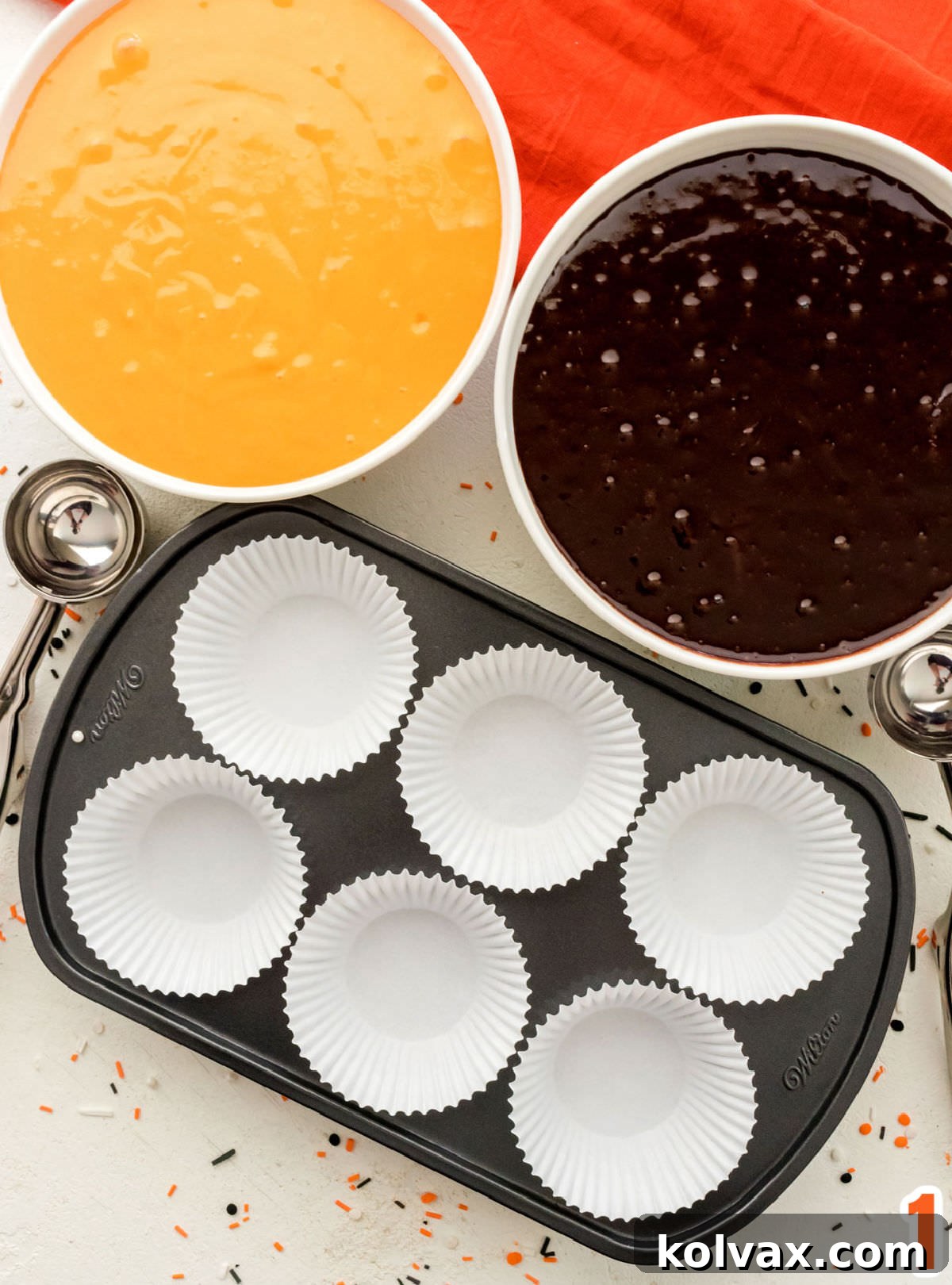 Closeup of two white bowls, one filled with dark brownie batter and the other with vibrant orange cake batter, ready for mixing and layering.