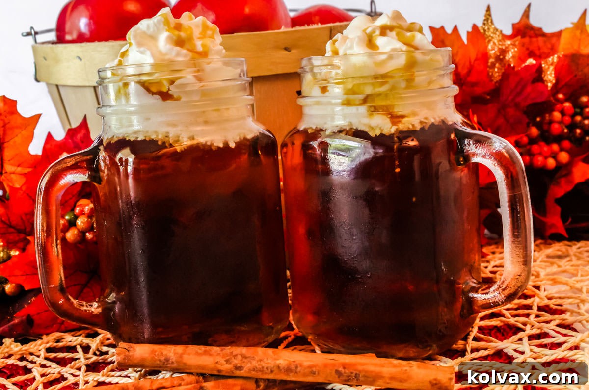 Two glass mugs filled with Caramel Apple Cider topped with Whipped Cream with two cinnamon sticks.
